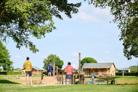 Familia disfrutando de zona de juegos de madera y cabañas en Camping Betuwe, Gelderland, Países Bajos.