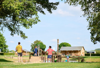Familie geniet van houten speelzone en hutten op Camping Betuwe vakantiepark in Gelderland, Nederland.