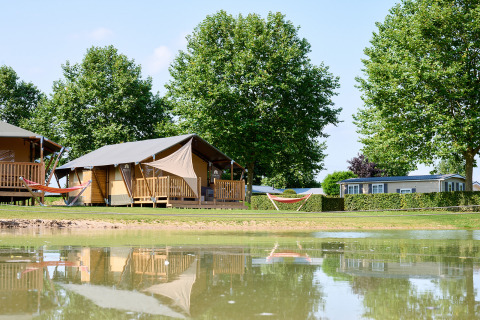 Tiendas glamping y casas móviles junto a un estanque en Camping Betuwe, parque vacacional en Gelderland, Países Bajos.