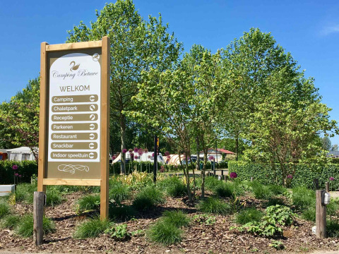 Cartel de entrada de Camping Betuwe en Gelderland, Países Bajos, rodeado de jardines y árboles verdes.
