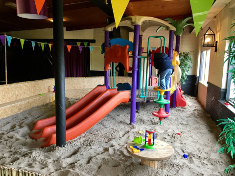 Parque infantil interior con toboganes, arena y niño jugando en Camping Betuwe, Gelderland, Países Bajos.