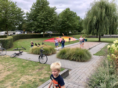 Børn leger på en legeplads med hoppepude og cykler i Camping Betuwe, Gelderland, Nederlandene.