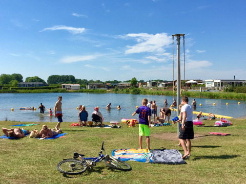 Familias disfrutando de un día soleado junto al lago en Camping Betuwe, parque vacacional de Gelderland.