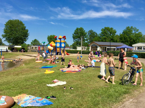 Familias y niños disfrutan del sol y la diversión junto al lago en Camping Betuwe, Gelderland, Países Bajos.