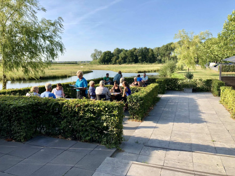 Terraza al aire libre en Camping Betuwe, parque vacacional en Gelderland, Países Bajos, con gente comiendo.