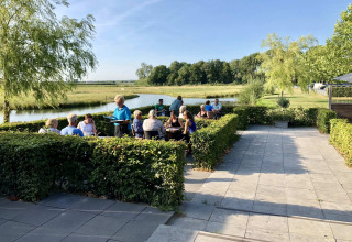 Buitenrestaurant bij Camping Betuwe, vakantiepark in Gelderland, Nederland, mensen dineren langs het water.