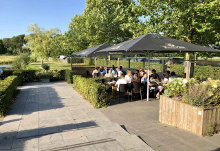 Openluchtterras bij Camping Betuwe in Gelderland, Nederland met mensen ontspannen onder grote parasols.