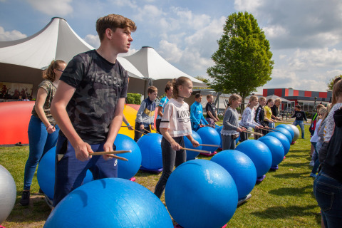 Niños participan en un taller de percusión al aire libre con grandes pelotas azules en Camping Betuwestrand, Gelderland.