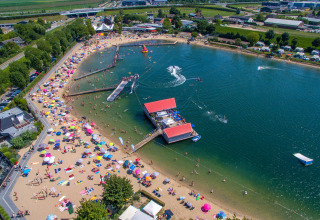 Luftfoto af Camping Betuwestrand i Gelderland, Holland, med strand, sø, parasoller og campister.