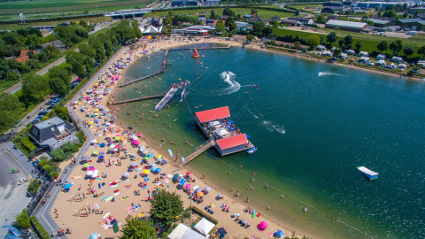 Vista aerea del Camping Betuwestrand in Gelderland, Paesi Bassi, con spiaggia, lago e molti campeggiatori.