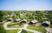 Luftfoto af Camping Betuwestrand i Gelderland, Holland, med hytter, grønne omgivelser og campingvogne.