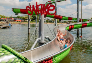 Kinderen glijden van een kleurrijke waterglijbaan aan het meer op Camping Betuwestrand in Gelderland, Nederland.