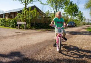 Une enfant souriante fait du vélo sur un chemin de gravier au Camping Betuwestrand, Gelderland, Pays-Bas.