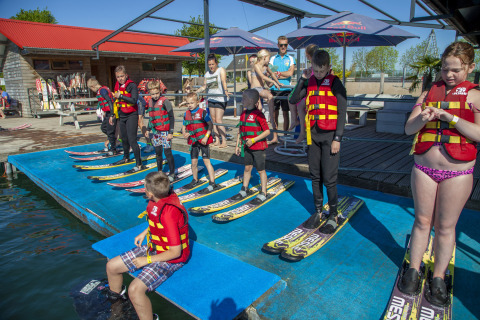 Niños con chalecos salvavidas y esquís acuáticos se preparan para esquiar en Camping Betuwestrand, Gelderland.