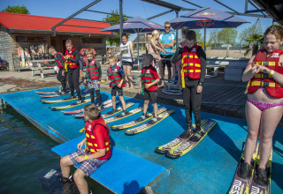 Bambini con giubbotti di salvataggio e sci d’acqua al Camping Betuwestrand, Gelderland, pronti a sciare.