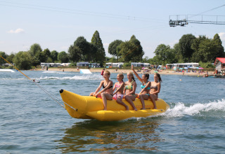 Vier kinderen rijden op een opblaasbare banaan op het meer bij Camping Betuwestrand, Gelderland, Nederland.