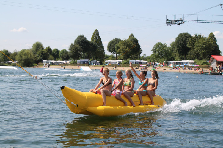 Vier kinderen varen op een opblaasbare banaan op het meer bij Camping Betuwestrand in Gelderland, Nederland.