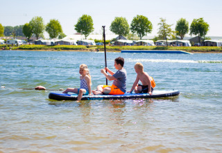 Kinderen spelen op een paddleboard aan het meer op Camping Betuwestrand vakantiepark in Gelderland.