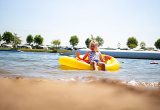 Une fille se détend sur un radeau gonflable jaune dans l'eau au Camping Betuwestrand, Gueldre, Pays-Bas.