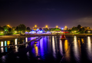 Nachtzicht op Camping Betuwestrand in Gelderland, Nederland, met verlichte tenten en reflectie in het water.