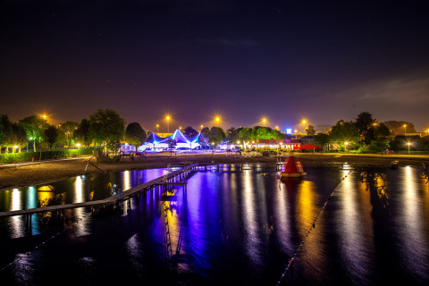 Night view of Camping Betuwestrand in Gelderland, Netherlands, showing lit tents reflected in the water.