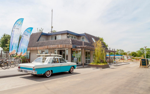 Entrada al Camping Betuwestrand en Gelderland, Países Bajos, con un coche clásico estacionado frente a la recepción.