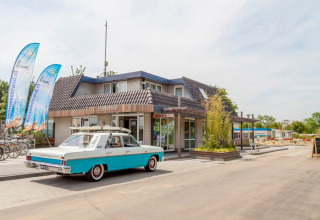 Ingang van Camping Betuwestrand in Gelderland, Nederland met een retro auto voor de receptie geparkeerd.