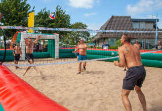 Gasten spelen beachvolley op het zand bij Camping Betuwestrand, Gelderland, Nederland, op een zonnige dag.