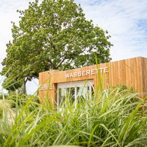 Holzgebäude mit Waschsalon und Toilette bei Camping Betuwestrand in Gelderland, Niederlande, umgeben von Natur.