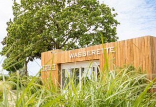 Modern wooden laundry and toilet facility at Camping Betuwestrand in Gelderland, Netherlands, amidst greenery.