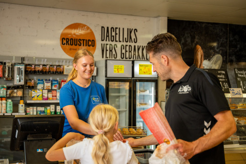 Vader en dochter doen boodschappen in de winkel van Camping Betuwestrand, Gelderland, Nederland, met glimlachend personeel.