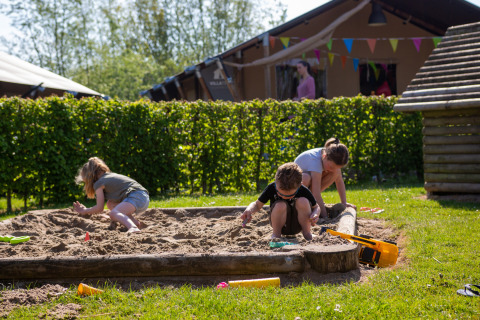 Børn leger i en sandkasse på Camping Betuwestrand, en feriepark i Gelderland, Holland, på en solrig dag.