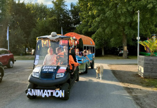 Animationswagen mit fröhlichen Gästen und Hund im Camping Borken am See, umgeben von Bäumen.