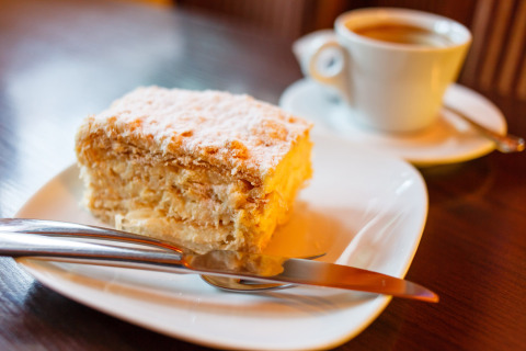 A layered pastry with powdered sugar on a plate with cutlery, coffee in the background at Camping Borken am See.
