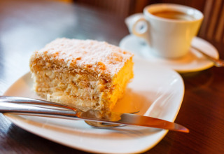 Une part de gâteau feuilleté saupoudrée de sucre glace, assiette avec couverts et café à Camping Borken am See.