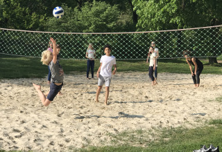 Niños y adultos juegan voleibol de playa en una cancha de arena en Camping Borken am See, Alemania.