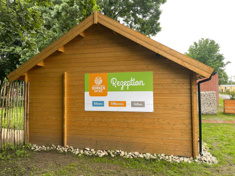 Cabaña de madera con cartel de 'Rezeption' en Camping Borken am See, parque vacacional en Renania del Norte-Westfalia.