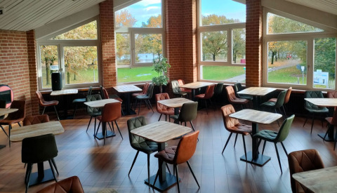 Cafetería luminosa con grandes ventanales, mesas de madera y sillas de colores en Camping Borken am See.