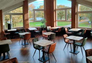 Bright, modern café space with colorful chairs, wooden tables, and large windows at Camping Borken am See.