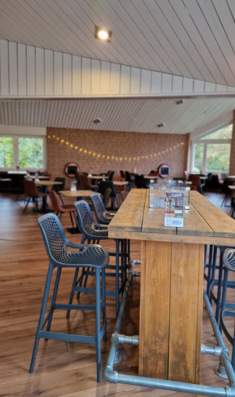 Zona de comedor moderna en Camping Borken am See con mesa de madera, taburetes y luces acogedoras en Alemania.