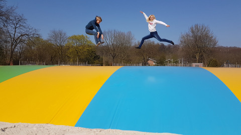 Dos niños saltan y juegan en una gran colchoneta inflable de colores en Camping Borken am See al aire libre.