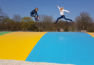 Two children jump and play on a large, colorful jumping pillow outdoors at Camping Borken am See holiday park.