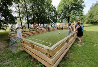 Børn og voksne leger på en lille fodboldbane med træbarrierer i ferieparken Camping Borken am See.