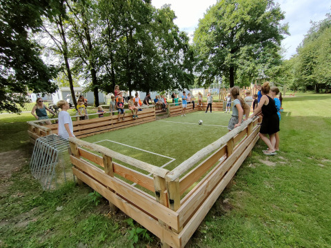 Børn og voksne leger på en lille fodboldbane med træbarrierer i ferieparken Camping Borken am See.