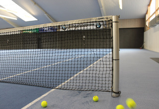 Campo da tennis al coperto con rete e palline a terra al Camping Borken am See, Germania.