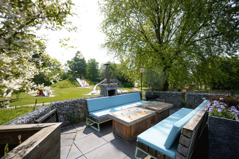 Outdoor seating area with blue benches, wooden tables, and playground view at Camping Borken am See, Germany.