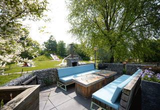 Zona de asientos al aire libre con bancos azules y vista a un parque infantil en Camping Borken am See, Alemania.