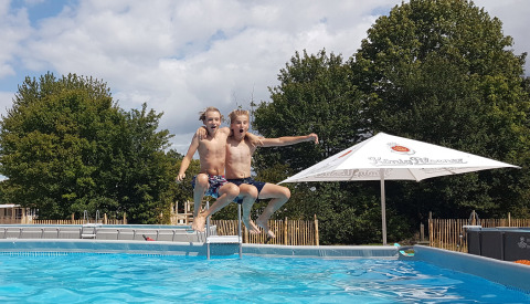 Twee jongens springen samen in een zwembad op Camping Borken am See in Noordrijn-Westfalen, Duitsland.