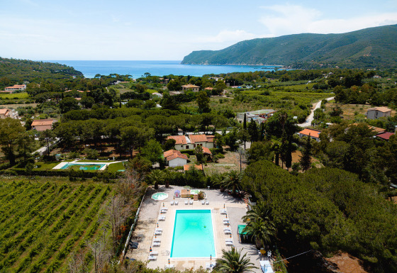 Luchtbeeld van Camping Casa dei Prati in Toscane, Italië, met zwembad, veel groen en de zee op de achtergrond.