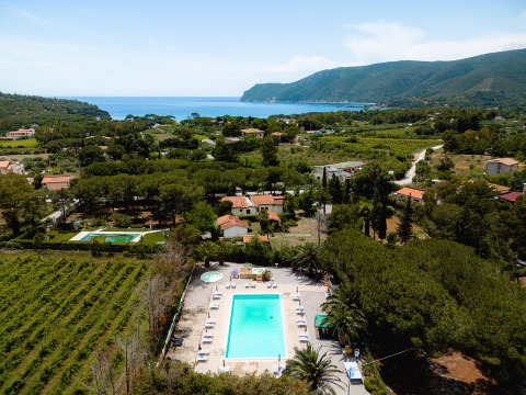 Aerial view of Camping Casa dei Prati holiday park in Tuscany, Italy, showing pool, trees, and sea in the distance.